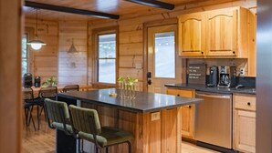 A wooden cabin interior with a kitchen area, a dining table with chairs, and a bar area with stools. - Amazing Mountain Views + Hot Tub (Blue Ridge)