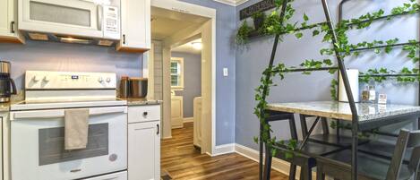 Una cocina con electrodomésticos blancos, una mesa de comedor con sillas y una pared cubierta de plantas trepadoras.