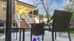 An outdoor patio area with a fire feature, wicker chairs, and a staircase leading to a porch. - Cozy 3bdrm 2ba mins from Downtown (Greensboro)