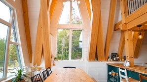 A dining area with a wooden table and chairs, a bench, and a view of the outdoors through large windows. - Waterfront Timber A-Frame Cabin on French River (French River)