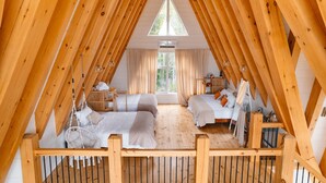 An attic bedroom with wooden beams, two beds, a window, and a hanging chair. - Waterfront Timber A-Frame Cabin on French River (French River)