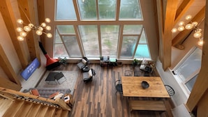 A spacious loft with a high ceiling, large windows, and a wooden interior. - Waterfront Timber A-Frame Cabin on French River (French River)