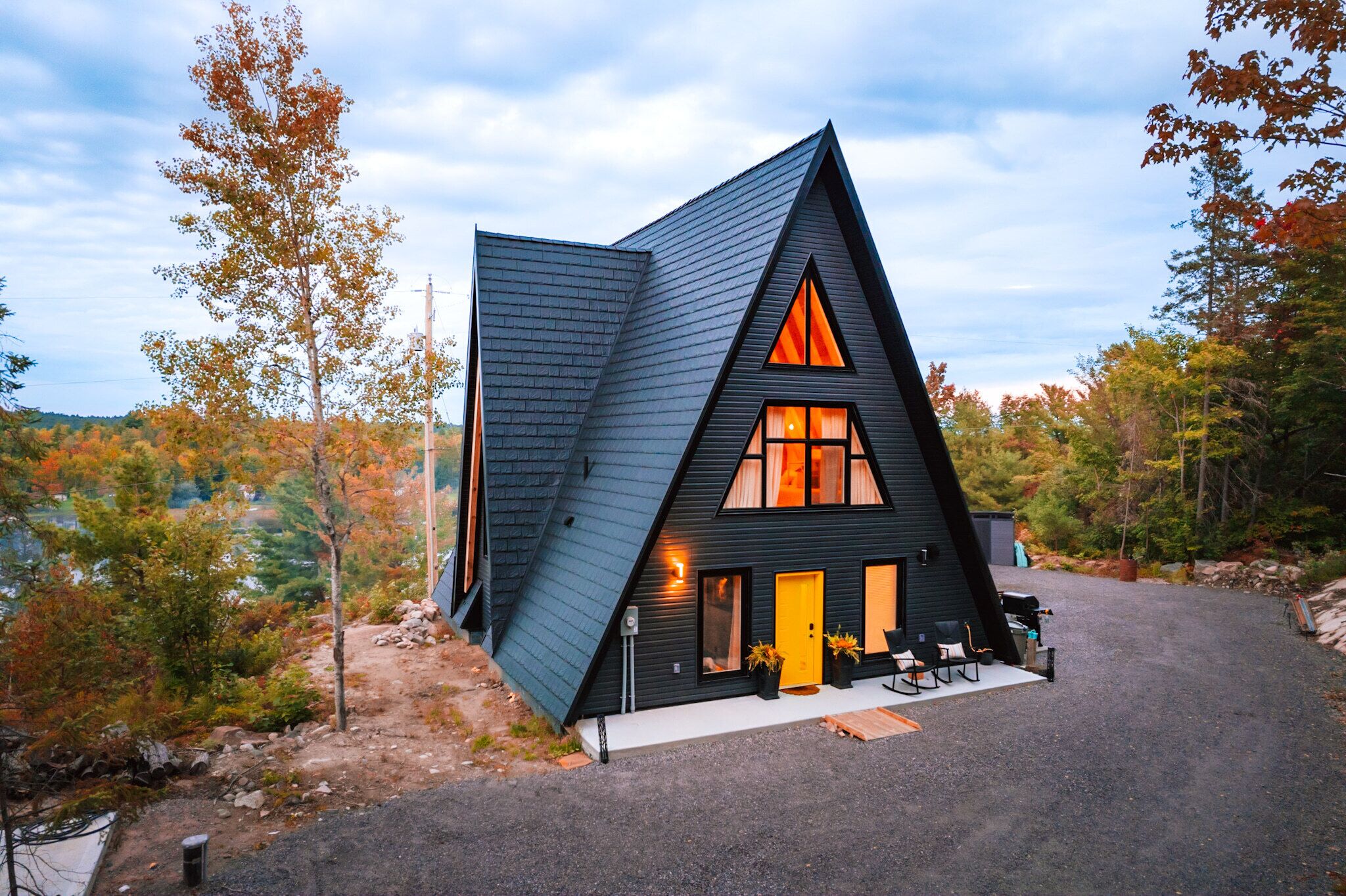 Une cabane moderne, aux couleurs sombres, dotée d’un toit à forte pente, de grandes fenêtres et d’un petit espace porche.
