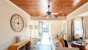 Una sala de estar moderna con techo de madera, un reloj de pared grande, un sofá, un banco y una mesa de centro.