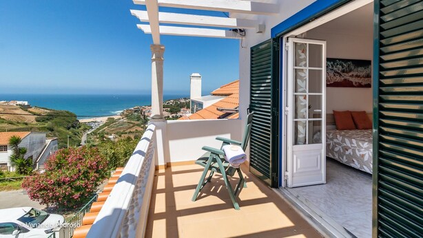 A balcony with a view of the sea, a bed with green shutters, and a chair with a towel. - Casa Sardine by Acasadascasas (Mafra)