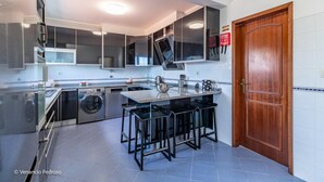 A modern kitchen with a central island, built-in appliances, and a wooden door. - Casa Sardine by Acasadascasas (Mafra)