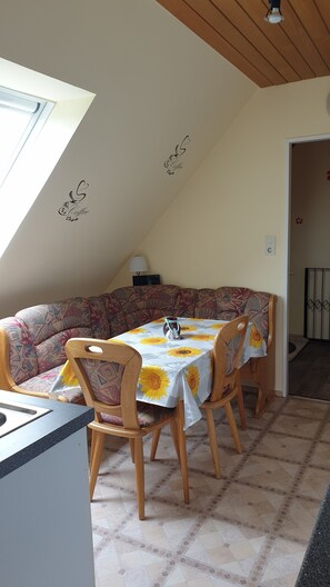 Comedor con una mesa cubierta con mantel de girasoles, rodeado de sofás estampados y sillas de madera.
