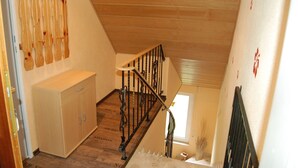 Una escalera de madera con barandilla metálica, un mueble de madera y una pequeña ventana.