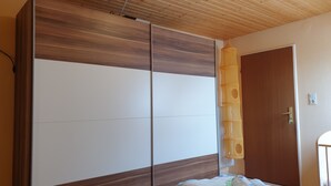 Un dormitorio con techo de madera, un armario con puertas correderas, una cama con manta blanca y azul, y una puerta de madera.