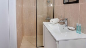 A modern bathroom with a glass shower enclosure, a white sink with a mirror, and beige tiled walls.