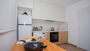 A compact kitchen with a wooden table, a stove, a washing machine, and a refrigerator.