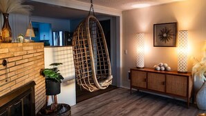 A cozy living room with a hanging chair, a fireplace, and a wooden cabinet. - Pacific City Riverfront Bungalow on Nestucca River! Dog friendly-Hot tub-Firepit (Pacific City)