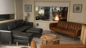 A modern living room with a sectional sofa, a brown leather couch, and a patterned ottoman. A wooden side table and a woven basket are also visible. - Pacific City Riverfront Bungalow on Nestucca River! Dog friendly-Hot tub-Firepit (Pacific City)