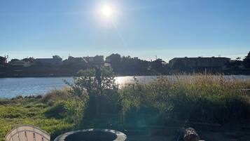 A clear sky with the sun shining, a body of water, and a fire pit with logs and a chair in the foreground.