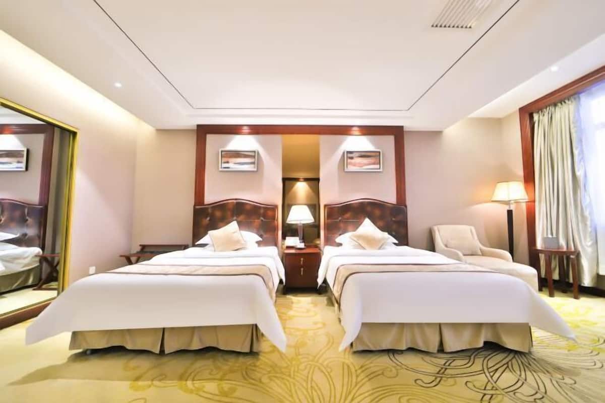 A hotel room with two beds, a chair, a desk, a lamp, and a mirror.