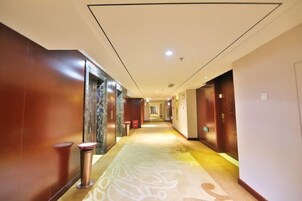 A hotel corridor with a marble wall, a patterned carpet, and a red trash bin.