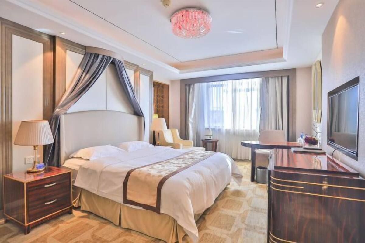 A hotel room with a large bed, a desk, a TV, and a chandelier.