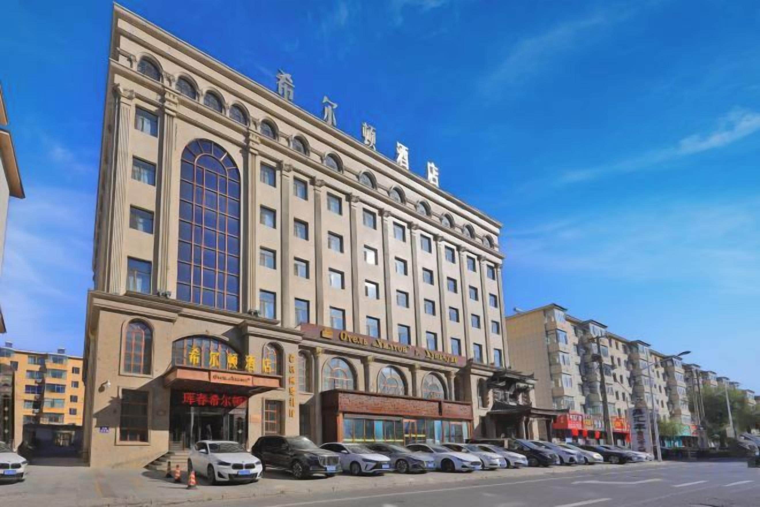 A multi-story hotel with a classic architectural style, featuring a large central arched window and multiple ground-level shops.