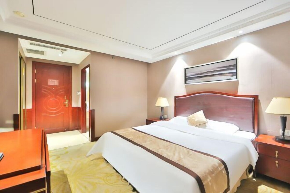A hotel room with a bed, bedside tables, a desk, and a door.