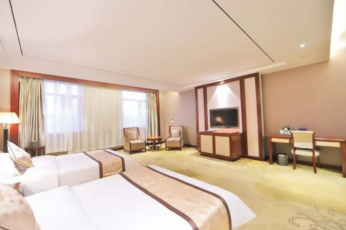 A hotel room with two beds, a TV, a desk, and a chair.