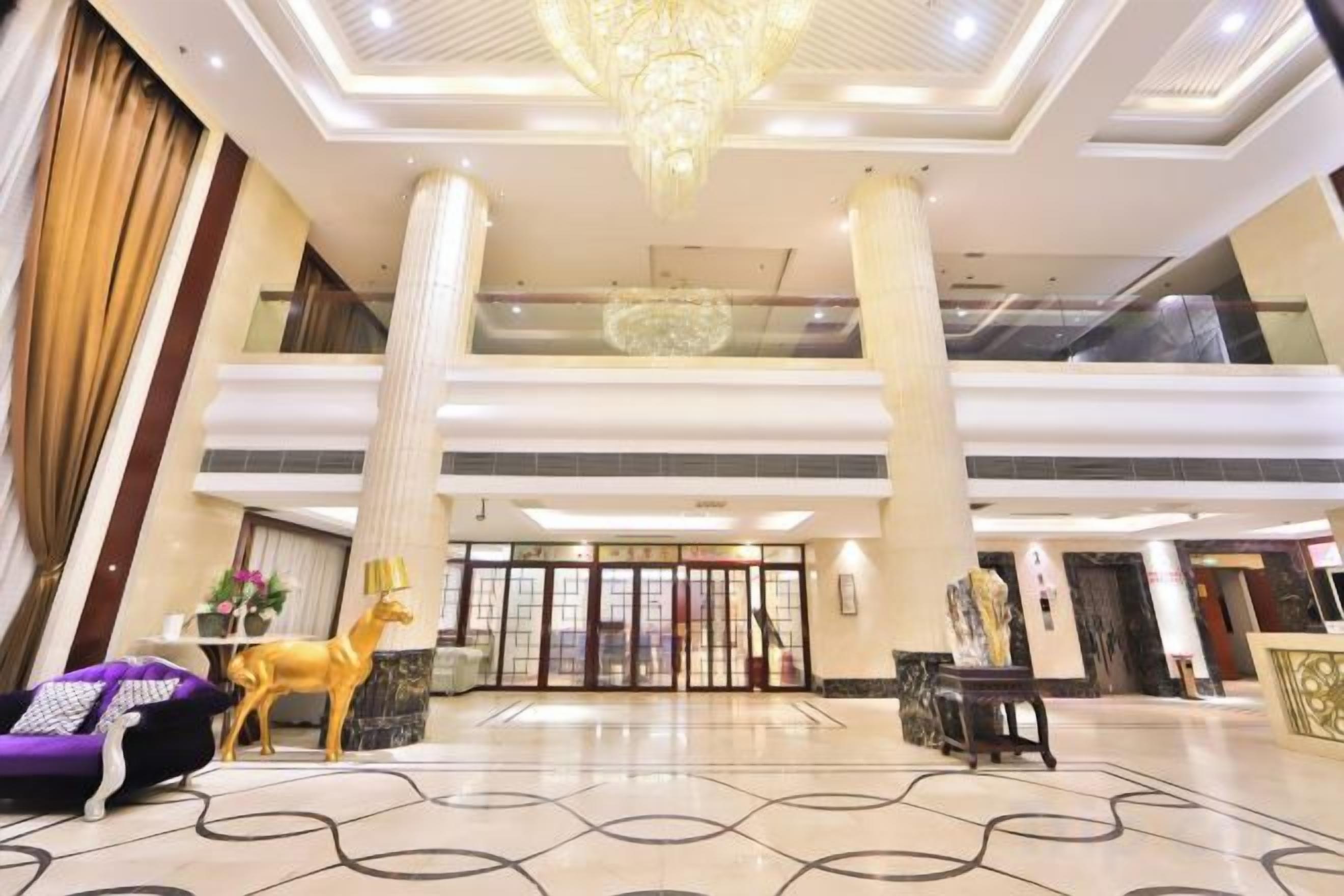A hotel lobby with a grand chandelier, a reception desk, and a statue of a deer.