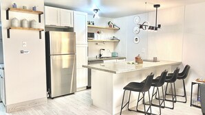 Une cuisine moderne avec des meubles blancs, un réfrigérateur en acier inoxydable et un îlot central doté de tabourets de bar.