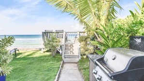 Un sentier menant à une maison de plage avec vue sur l’océan, un barbecue et une végétation luxuriante.