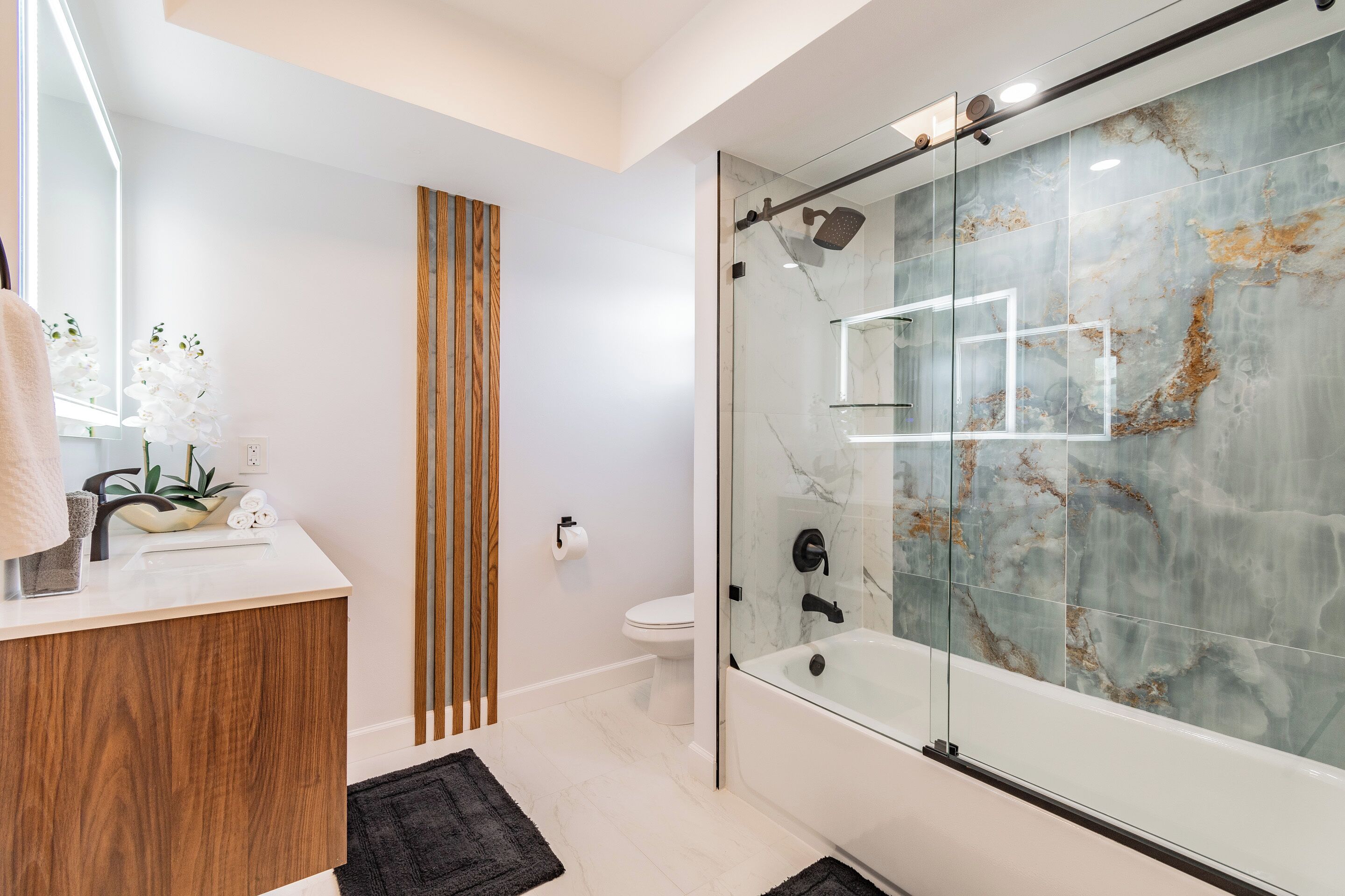 A modern bathroom with a glass-enclosed shower, a wooden vanity, and a marble backsplash.