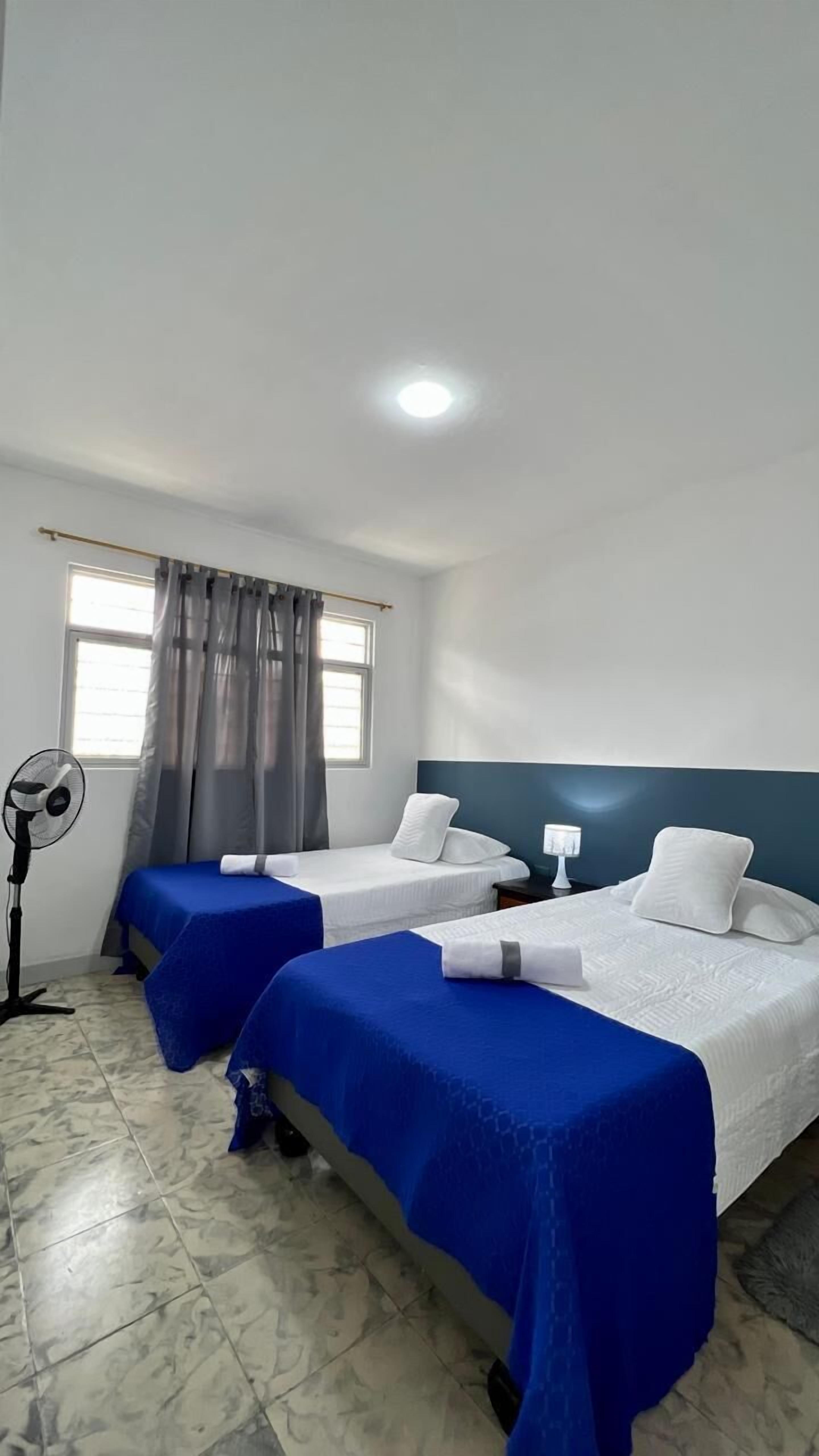 Habitación de hotel con dos camas, un ventilador y una ventana con cortinas.