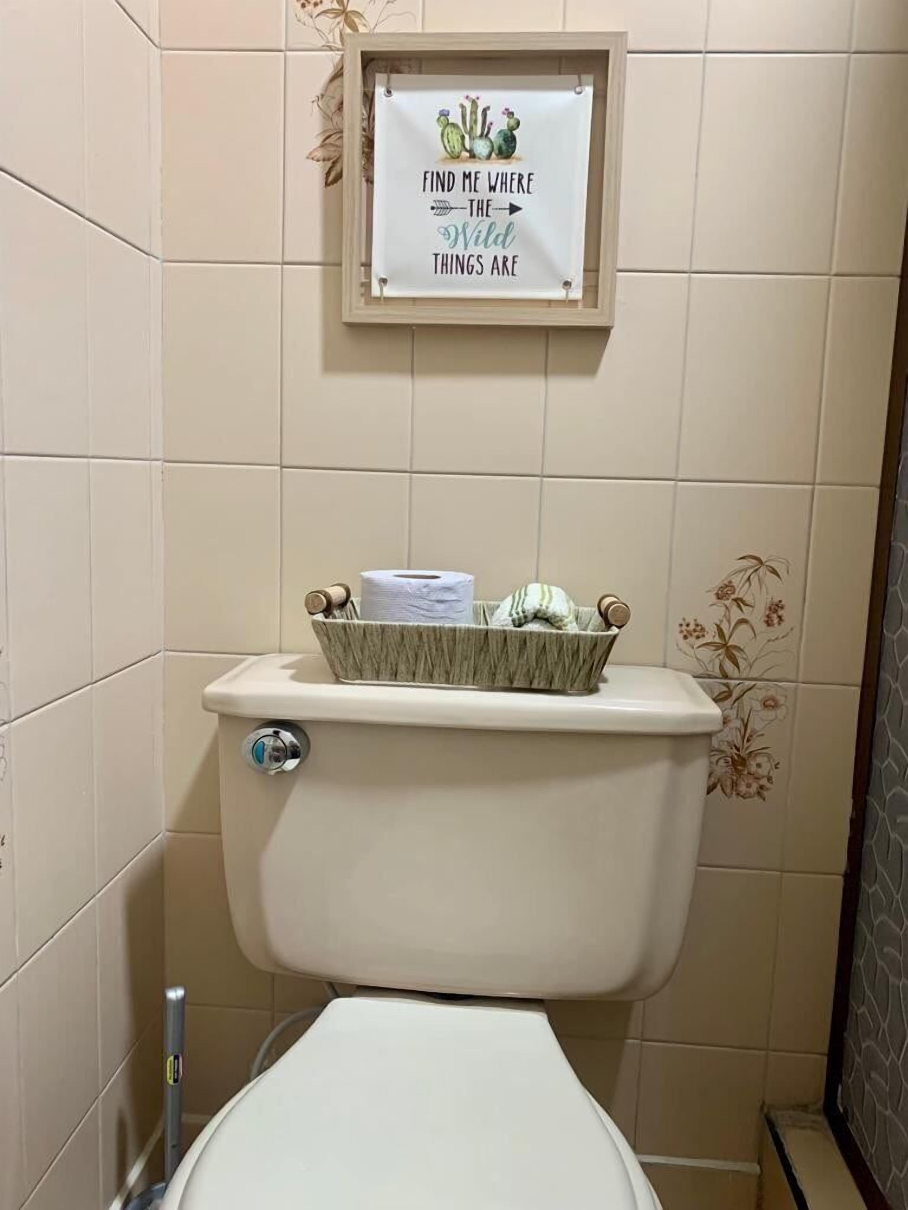 Eine Toilette mit einem Korb voller Pflegeprodukte und einem gerahmten Schild darüber.