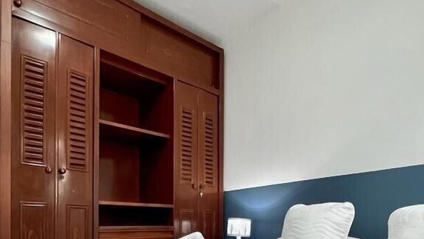 A hotel room with a large wooden wardrobe, a neatly made bed with white linens, and a blue patterned bedspread. - Casa Nawi (Cali)