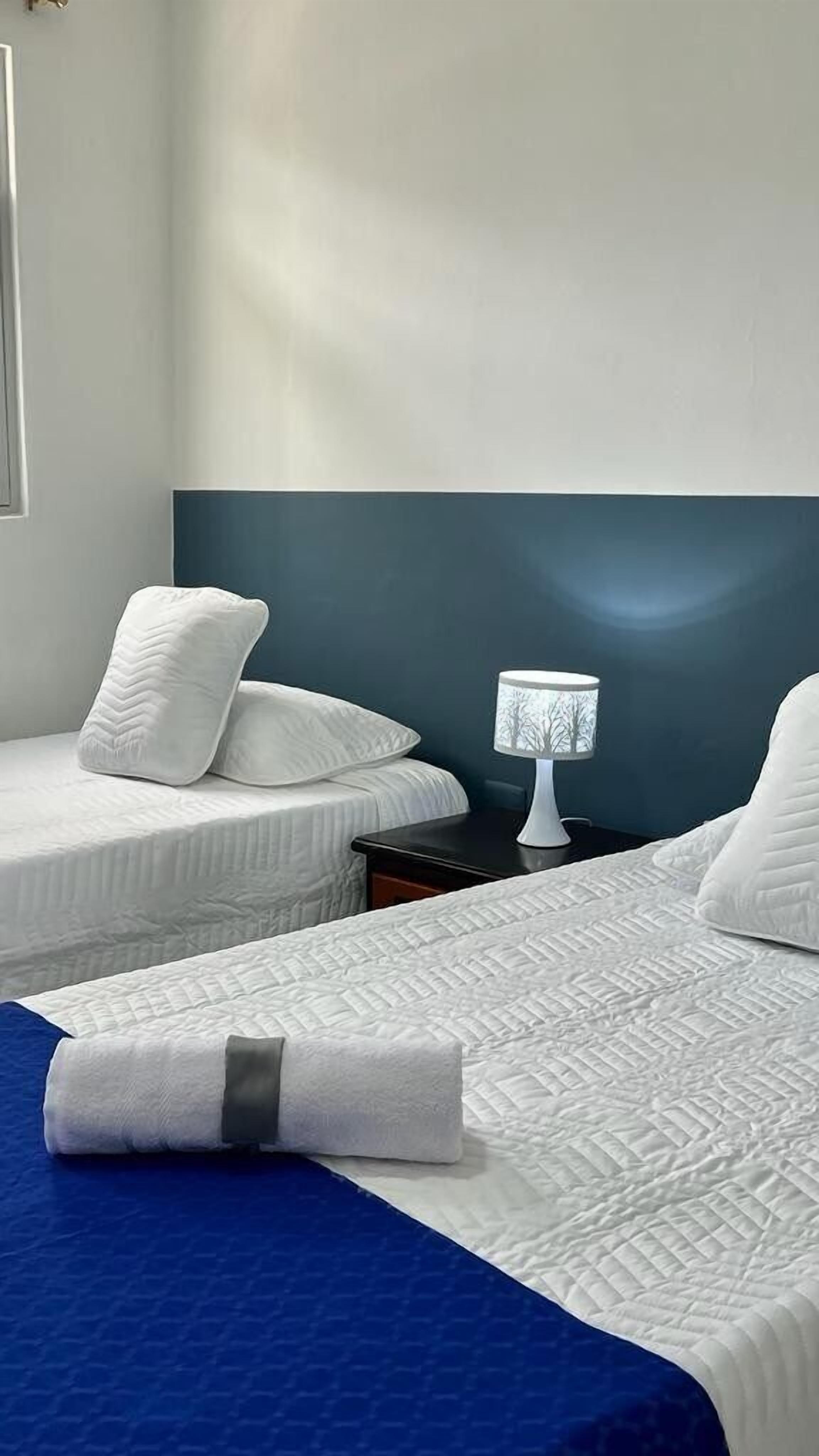 Une chambre d’hôtel avec deux lits, une table de chevet et une lampe.