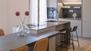 Ett modernt kök med en central köksö, barstolar och en hängande lampa.