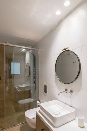 Ein modernes Badezimmer mit Duschkabine aus Glas, einem weißen Waschbecken mit Spiegel darüber und einer Toilette.