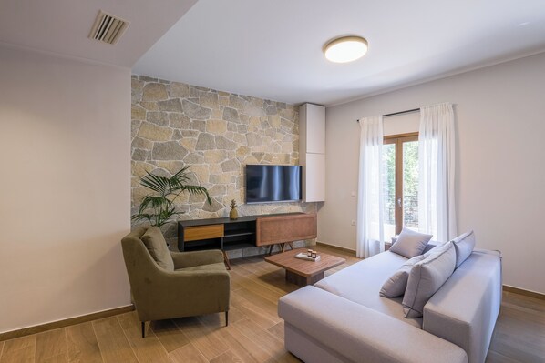 Ein modernes Wohnzimmer mit Steinakzentwand, einem Flachbildfernseher, einer Couch, einem Sessel und einem Couchtisch.