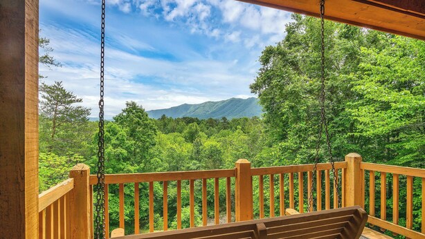 A wooden deck with a swing chair overlooking a forested mountain landscape. - Enjoy this cozy home with a wrap around porch, near the Smoky Mountains (Townsend)