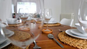 A dining table set with white plates, bowls, and wine glasses, with woven placemats and a spoon.