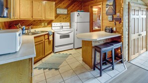 A cozy kitchen with wooden cabinets, a stove, a refrigerator, and a bar area. - Okauchee Lake Vacation Rental w/ Boat Dock! (Oconomowoc)