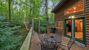 A wooden cabin with a deck, a table with chairs, and a large window.