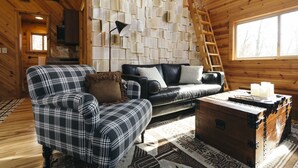 A cozy cabin interior with a plaid armchair, a leather sofa, and a wooden chest.