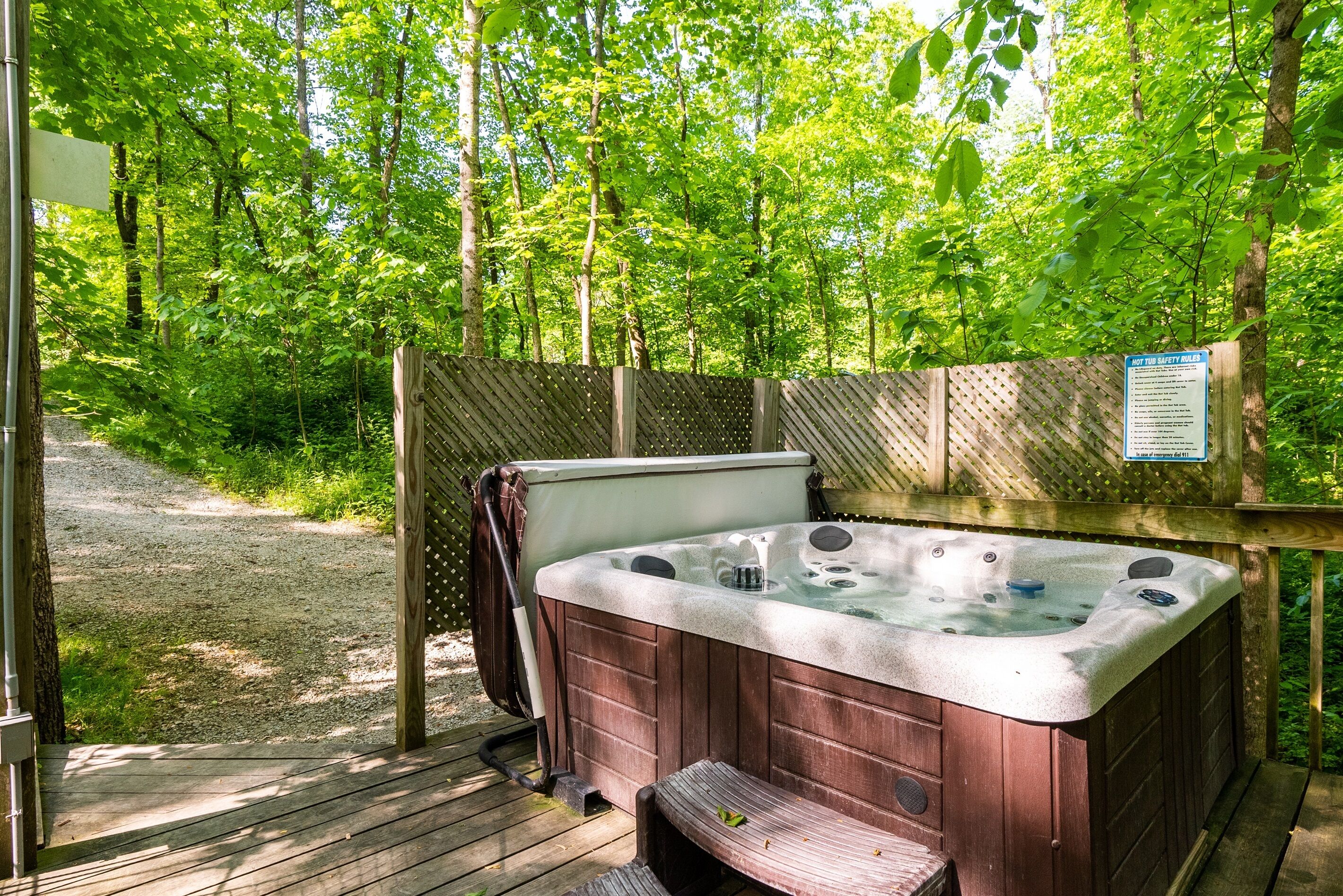 Ein Whirlpool auf einer Holzdielen-Terrasse, umgeben von einem Holzzaun und üppiger Vegetation.