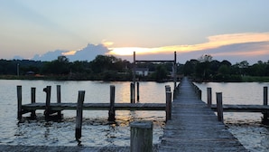 Eine hölzerne Pier, die sich in ruhiges Wasser erstreckt, mit einem Sonnenuntergang im Hintergrund.