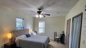 Ein Schlafzimmer mit einem Bett, Nachttischen, einem Deckenventilator und zwei Fenstern mit Jalousien.
