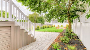 Une terrasse en bois avec une balustrade blanche, un chemin en pierre et un espace jardin agrémenté de paillis et de plantes.