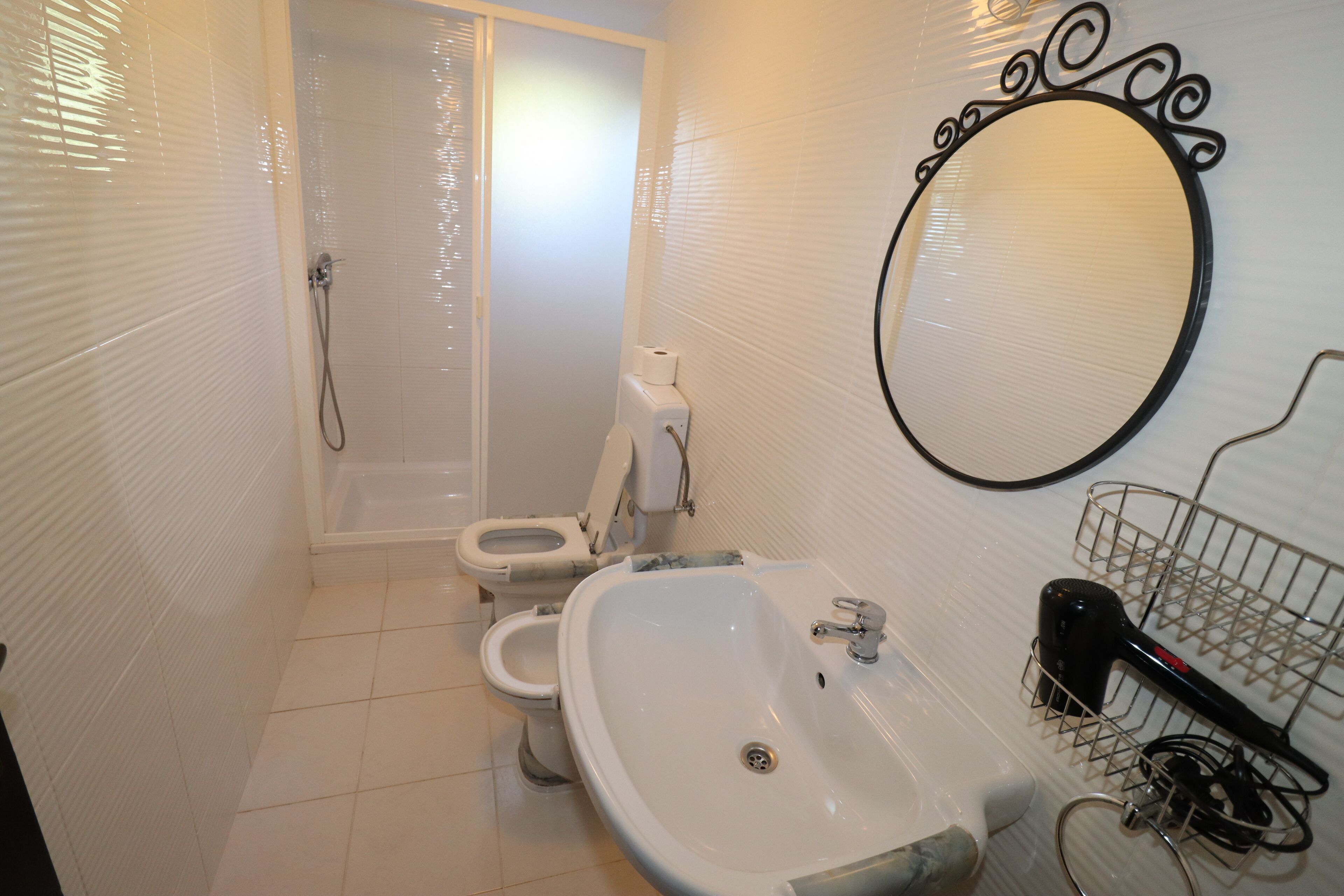 Et badeværelse med toilet, bidet, vask og spejl.