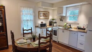 Une cuisine moderne avec des meubles blancs, une cuisinière, un four à micro-ondes et un coin repas avec des chaises en bois et une table dressée pour deux personnes.