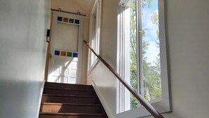 Un escalier avec une rampe en bois, des murs blancs et une fenêtre donnant sur les arbres.