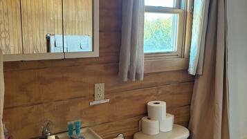 A wooden-paneled bathroom with a sink, mirror, toilet, and window with curtains.