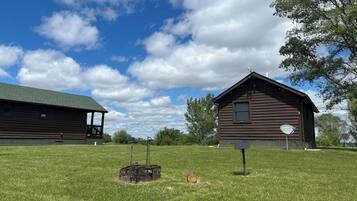 Une cabane en bois rustique, surmontée d’un toit vert, entourée d’un champ verdoyant bien entretenu et d’arbres.
