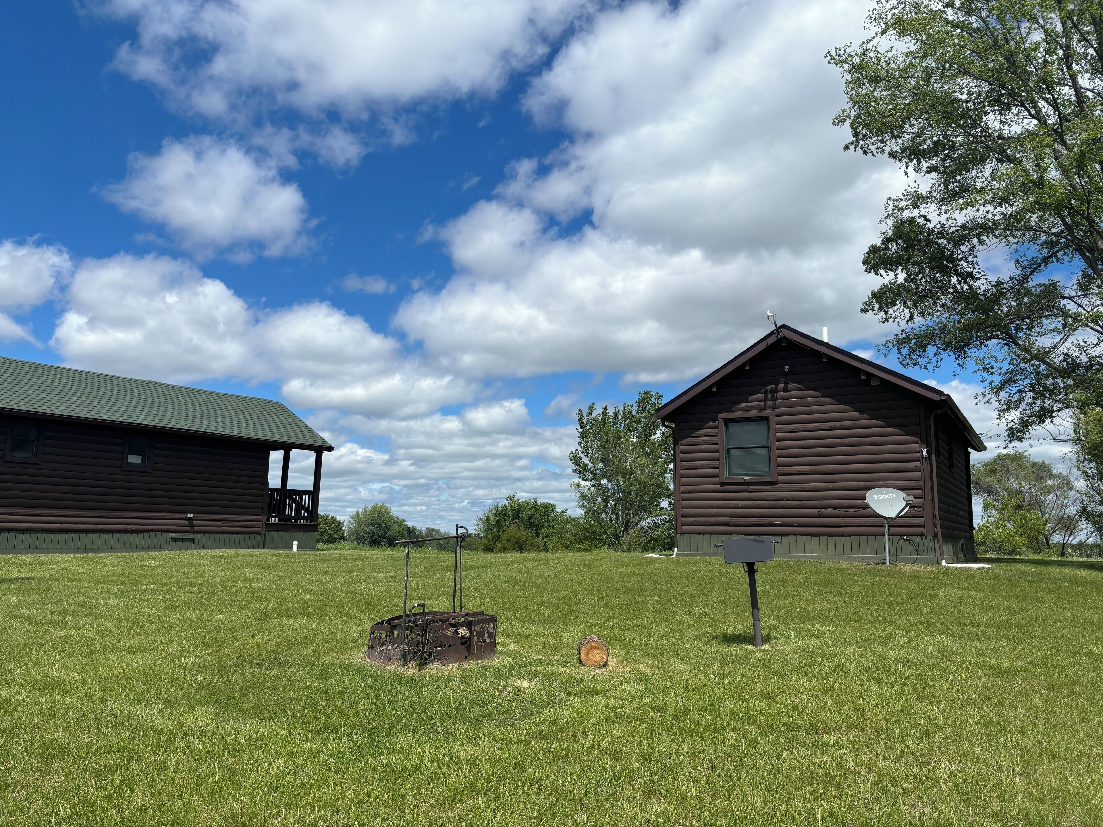 A rustic wooden cabin with a green roof, surrounded by a well-maintained grassy field and trees.